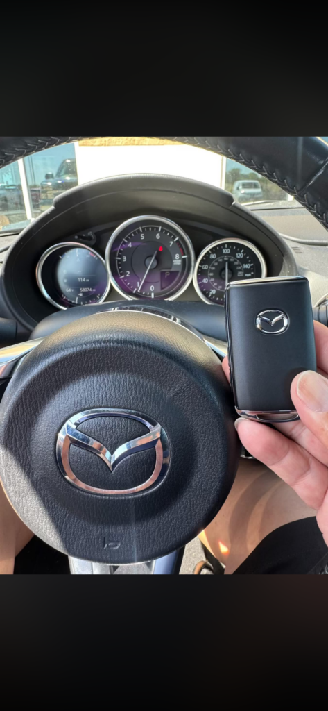 Replacement Mazda proximity key held in front of the steering wheel after a 2023 CX-5 all-keys-lost job in McKinley Park, Chicago.